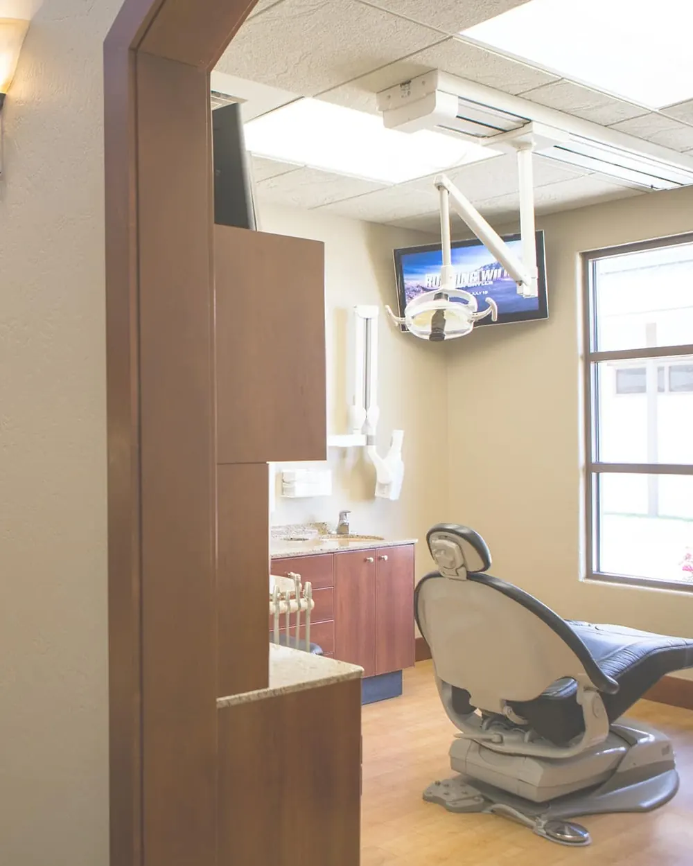A treatment room with its dental chair and a ceiling-mounted chairside screen.
